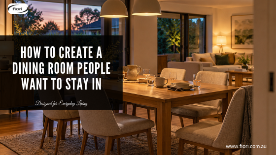 Warm Australian dining room at dusk with a timber table, comfortable upholstered chairs, used glasses and softly illuminated adjoining living space.